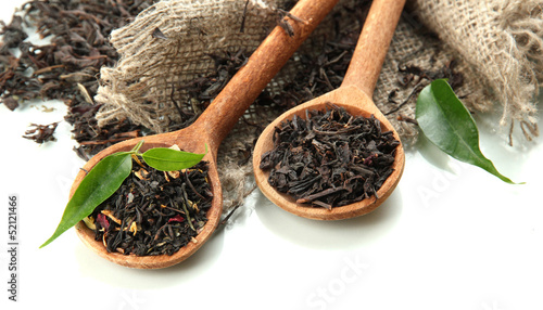 Photo: Dry tea with green leaves in wooden spoons, isolated on white Dry tea with green leaves in wooden spoons, isolated on white