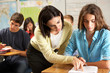 Teacher Helping Female Pupil Studying At Desk In Classroom