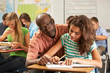 Teacher Helping Female Pupil Studying At Desk In Classroom