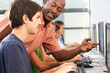 Teacher Helping Students Working At Computers In Classroom