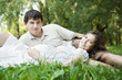 Pregnant wife and her husband lying on green grass