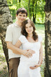 Pregnant wife and her husband in park next to trees