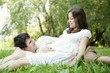 Pregnant wife and her husband lying on green grass