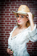 young woman with  straw hat and white kaftan against a brick wal