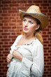 young woman with  straw hat and white kaftan against a brick wal