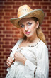 young woman with  straw hat and white kaftan against a brick wal