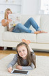 Foto: Smiling little girl using tablet while her mother is reading Smiling little girl using tablet while her mother is reading