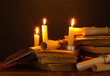 Pile of old books with candle and scroll in dark
