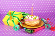 Colorful birthday cake with candle and gifts on pink background