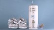 Baby shoes falling beside baptism candle on blue background