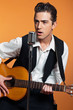 Retro country singer with guitar wearing black suit. Studio shot