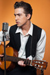 Retro country singer with guitar wearing black suit. Studio shot
