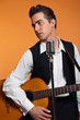 Retro country singer with guitar wearing black suit. Studio shot