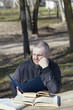 Foto: Tired man reading a book outdoors on a bench Tired man reading a book outdoors on a bench
