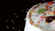 Colourful sprinkles pouring onto iced cake with candy