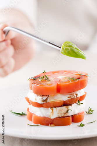 Photo: Hand serving a basil leaf on mozzarella and tomato slices close- Hand serving a basil leaf on mozzarella and tomato slices close-
