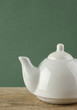 White teapot on old wooden table over green background