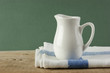 White jug and dishcloth on old wooden table over green backgroun