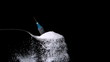 Syringe falling onto spoon of sugar on black background