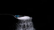 Syringe falling onto spoon full of sugar on black background