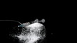 Needle falling onto spoon full of sugar on black background