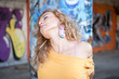 Happy hip teenage blonde girl standing by graffiti wall