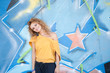 Happy hip teenage blonde girl standing by graffiti wall