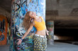 Happy hip teenage blonde girl standing by graffiti wall