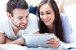 Photo: Couple with digital tablet lying on bed Couple with digital tablet lying on bed