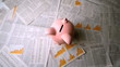 Pink piggy bank falling over sheets of paper