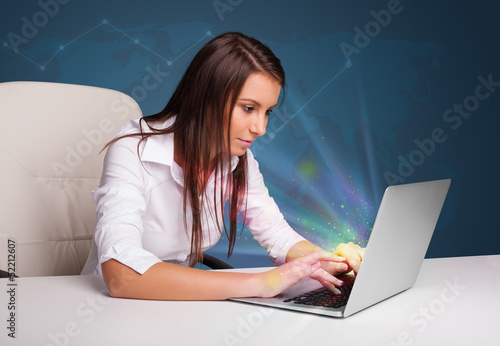 Photo: Beautiful woman sitting at desk and typing on laptop with abstra Beautiful woman sitting at desk and typing on laptop with abstra