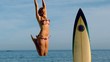 Blonde woman jumping beside her surfboard