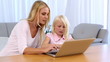 Mother and daughter sitting at table and using laptop