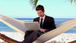 Businessman typing on his laptop in a hammock and smiling
