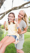 Portrait of happy mother pushing her daughter on a swing