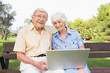 Portrait of old couple in the park using a laptop