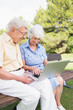 Smiling elderly couple in the park using a laptop