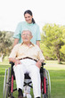 Nurse pushing elderly man through the park