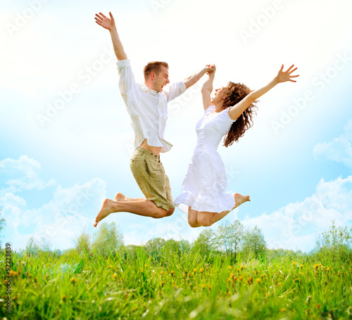Photo: Happy Couple Outdoor. Jumping Family on Green Field Happy Couple Outdoor. Jumping Family on Green Field