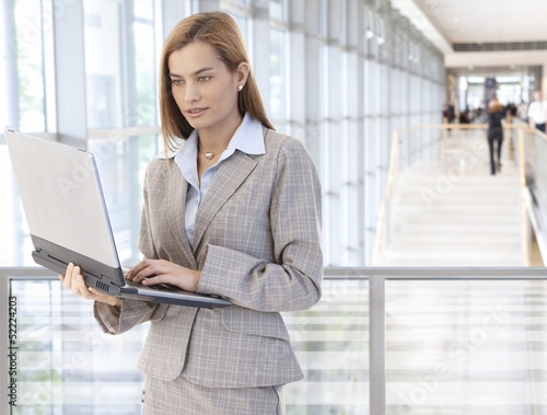 Photo: Businesswoman using laptop in office lobby Businesswoman using laptop in office lobby