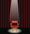 A directors chair on a stage with a red curtain and spotlight