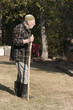 old man with kufi hat and stick walking on the garden