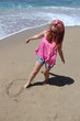 Beautiful rehead young woman drawing heart in the sand