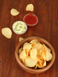 Potato chips  in wooden bowl and sauces, on wooden background