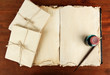 Open old book, letters and ink pen on wooden background