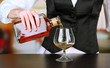 Barman hand with bottle of cognac  pouring drink into glass,
