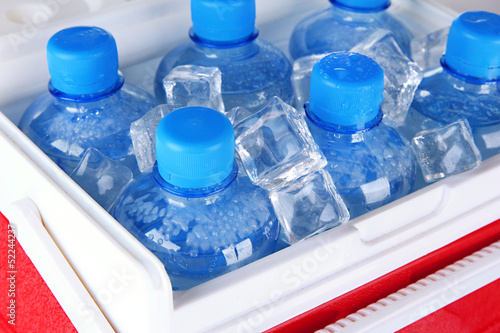 Photo: Bottles of water and ice cubes in traveling refrigerator, close Bottles of water and ice cubes in traveling refrigerator, close