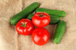 Tasty green cucumbers and red tomatoes on sackcloth background