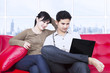 Couple looking at laptop in apartment on red sofa
