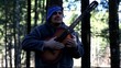 Man playing guitar in the woods leaning against tree